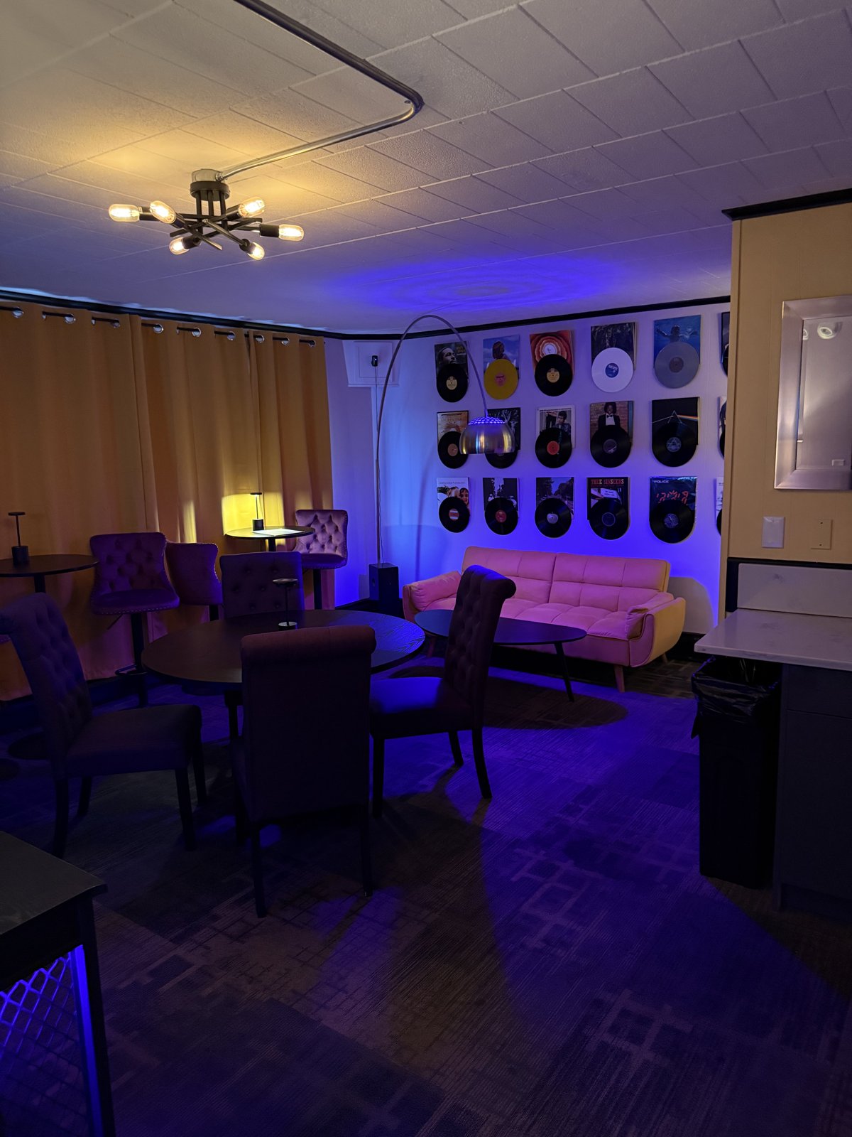 The Vinyl Room — wall of vinyl records with pink sofa under blue mood lighting
